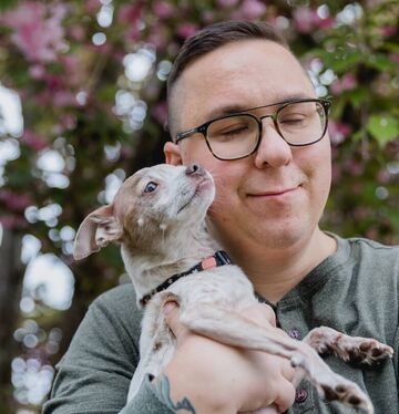 Man with glasses holding a small dog and smiling with his eyes closed