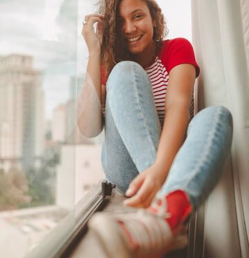 A smiling woman sits casually by the window